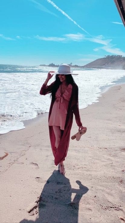 A woman in pink dress and hat walking on the beach.