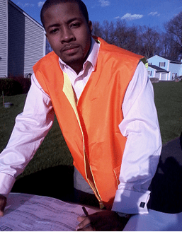 A man in an orange vest standing on the grass.